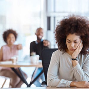 Upset woman at the desk while colleagues in the background point and laugh symbolizing Gender Discrimination -  Levian Law