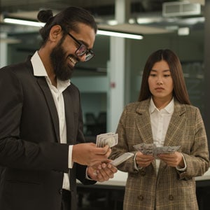 Man counting money with a smile while a woman beside him looks concerned, highlighting Gender Pay Discrimination   Levian Law